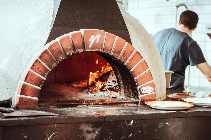 A pizza maker working at the mouth of a brick wood oven