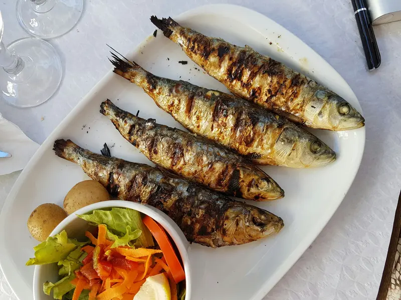 Grilled sardines on a white plate with potatoes and salad